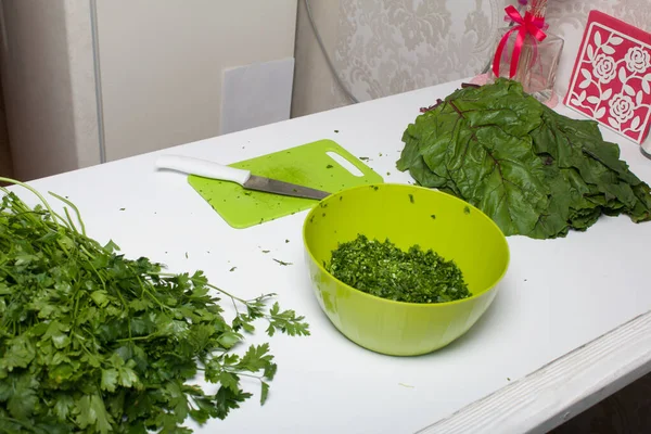 Harvesting greens for the winter. Parsley and beet tops on the table surface. Cutting Board and knife. In the container, crushed parsley.