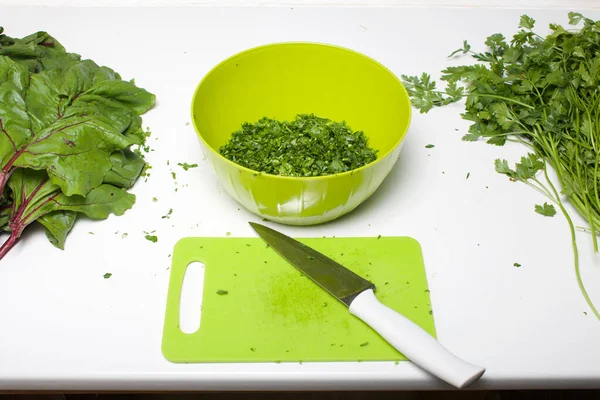 Harvesting greens for the winter. Parsley and beet tops on the table surface. Cutting Board and knife. In the container, crushed parsley.