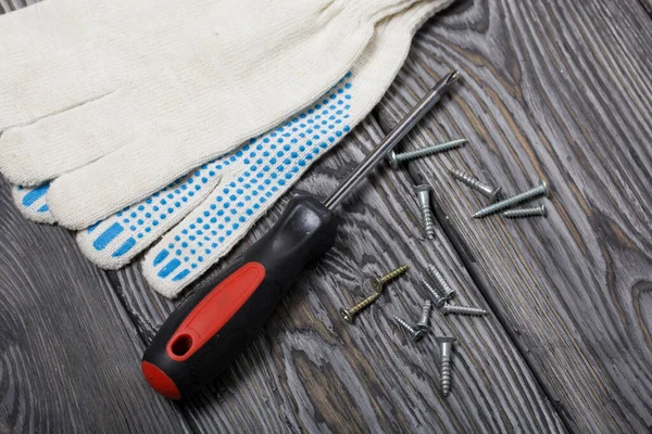 A screwdriver, work gloves, and a handful of screws. On painted pine boards.