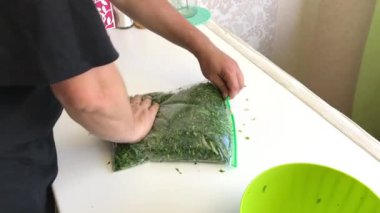 Adam vakum torbasını ezilmiş maydanozla dolduruyor ve içindeki havayı sıkıyor. Donmak için yeşiller. Sağdan çekiliyor.