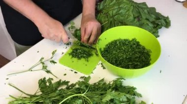 Adamın biri doğrama tahtasındaki bıçakla maydanoz kesiyor. Sonra da onu bir konteynıra koyuyor. Yanında da maydanoz ve pancar var..