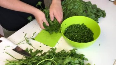 Adam maydanozu keser ve bir konteynıra koyar. Yanında da maydanoz ve pancar var.