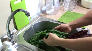 Bir adam mutfak yapraklarının üstündeki musluğun altını yıkıyor. Temiz yapraklar lavabonun sağına konur..
