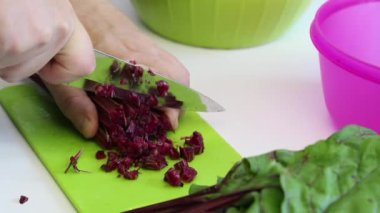 Adamın biri şeker pancarının tepelerini bıçakla kesiyor. Kesme tahtasında. Sonra da bir konteynıra koyuyor. Yakından çekilmiş..