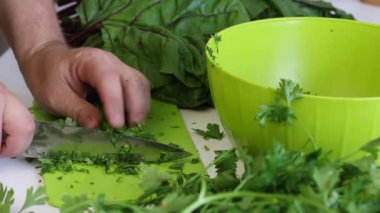 Bir adam, maydanozu kesme tahtasının üzerinde bıçakla dilimleyip bir konteynıra koyar. Masanın yanında bir sürü maydanoz ve pancar var. Sağdan çekiliyor..
