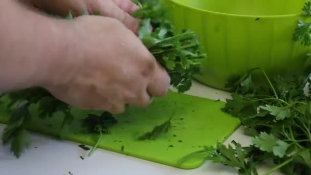 A man slices parsley. With a knife on the cutting Board. Next to the table there is a lot of parsley and beet tops. Close up. — Stock Video