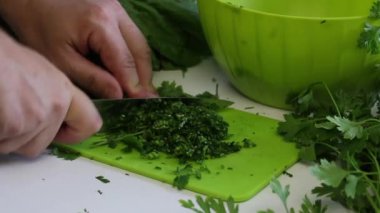 Bir adam, maydanozu kesme tahtasının üzerinde bıçakla dilimleyip bir konteynıra koyar. Masanın yanında bir sürü maydanoz ve pancar var. Kapat..