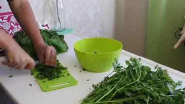 Adamın biri doğrama tahtasındaki bıçakla maydanozu dilimliyor. Bir konteynıra koyuyor. Masanın yanında bir sürü maydanoz ve pancar var..