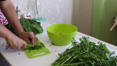 Adamın biri doğrama tahtasındaki bıçakla maydanozu dilimliyor. Masanın yanında bir sürü maydanoz ve pancar var..