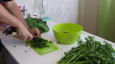 Adamın biri doğrama tahtasındaki bıçakla maydanozu dilimliyor. Masanın yanında bir sürü maydanoz ve pancar var.