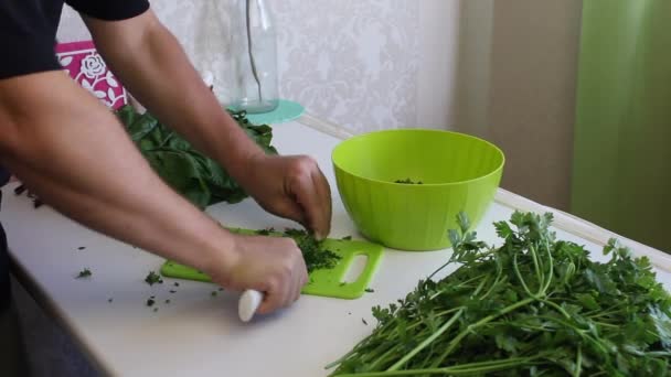 A man slices parsley with a knife on a cutting Board and puts it in a container. Next to the table there is a lot of parsley and beet tops. — Stock Video