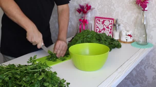 Muž krájí petržel. S nožem na prkně. Vedle stolu je spousta petržele a řepy. — Stock video