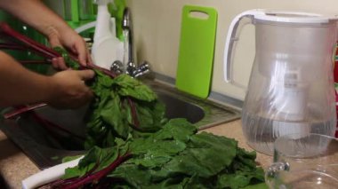 Bir adam mutfak musluğunun altındaki pancar yapraklarını yıkıyor. Aşırılığı bıçakla keser..