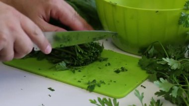 Bir adam, maydanozu kesme tahtasının üzerinde bıçakla dilimleyip bir konteynıra koyar. Masanın yanında bir sürü maydanoz ve pancar var. Kapat..