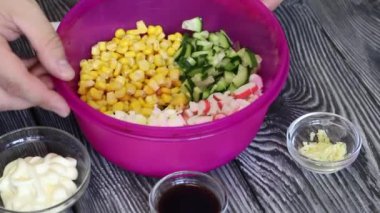 Bir adam elinde salata malzemesi olan bir konteynırı çevirir. Salata hazırlamak için yengeç çubukları, tavuk yumurtası ve sebze. Boyalı çam ağaçlarında yatıyorlar..