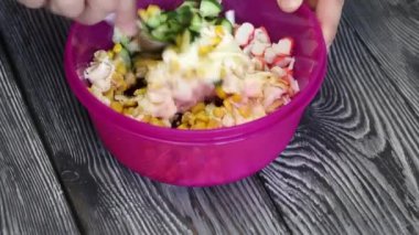 Bir adam salata malzemelerini bir kabın içinde karıştırıyor. Salata hazırlamak için yengeç çubukları, tavuk yumurtası ve sebze. Boyalı çam ağaçlarında yatıyorlar..