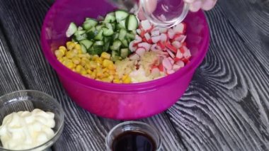 Bir adam salata malzemelerine sarımsak, sos ve mayonez ekler. Salata hazırlamak için yengeç çubuğu, tavuk yumurtası ve sebze..