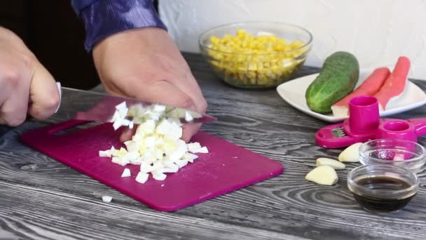 A man cuts a boiled egg on a cutting board. Crab sticks, chicken eggs and vegetables for salad preparation. They lie on painted pine boards — Stock Video