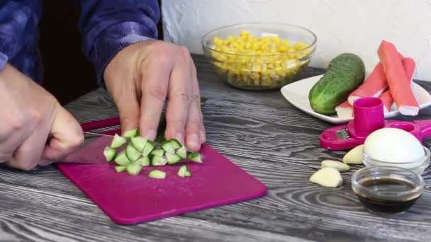 Egy férfi uborkát vág a vágódeszkán. Rákrudak, tyúktojás és zöldség salátakészítéshez. Festett fenyődeszkákon fekszenek. — Stock videók