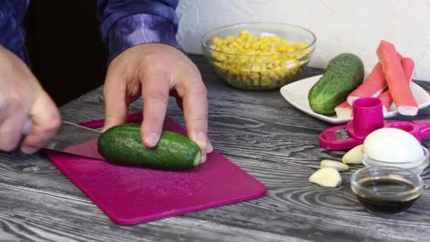 En man klipper en gurka på en skärbräda. Krabbpinnar, hönsägg och grönsaker för salladsberedning. De ligger på målade tavlor.. — Stockvideo