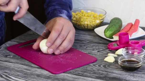 Ein Mann schneidet ein gekochtes Ei auf einem Schneidebrett. Krabbenstangen, Hühnereier und Gemüse für die Salatzubereitung. Sie liegen auf bemalten Kiefernbrettern. — Stockvideo