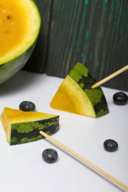 Çubuklardaki sarı karpuz parçaları. Yakınlarda yabanmersini var..