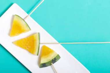 Çubuklardaki sarı karpuz parçaları. Tabağa uzan. Nane renginde bir yüzey üzerindeki tabaka.