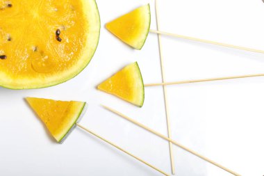 Çubuklardaki sarı karpuz parçaları. Beyaz bir yüzeyde plaka.