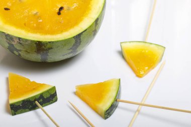 Çubuklardaki sarı karpuz parçaları. Beyaz bir yüzeyde plaka.