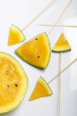Çubuklardaki sarı karpuz parçaları. Beyaz bir yüzeyde plaka.