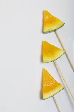 Çubuklardaki sarı karpuz parçaları. Beyaz bir yüzeyde plaka.