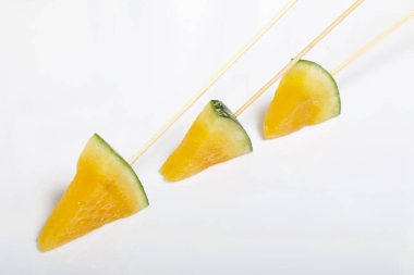 Çubuklardaki sarı karpuz parçaları. Beyaz bir yüzeyde plaka.