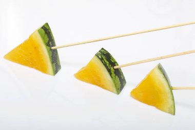 Çubuklardaki sarı karpuz parçaları. Beyaz bir yüzeyde plaka.