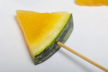 Çubuklardaki sarı karpuz parçaları. Beyaz bir yüzeyde plaka.