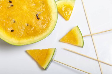 Çubuklardaki sarı karpuz parçaları. Beyaz bir yüzeyde plaka.