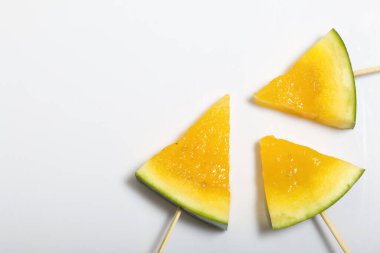 Çubuklardaki sarı karpuz parçaları. Beyaz bir yüzeyde plaka.