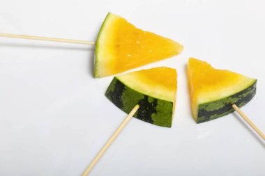 Çubuklardaki sarı karpuz parçaları. Beyaz bir yüzeyde plaka.