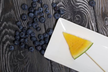 Şiş üzerinde sarı karpuz parçaları. Tabağa uzan. Tabak boyalı çam ağaçlarında.