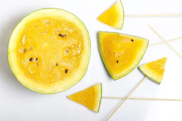 Çubuklardaki sarı karpuz parçaları. Beyaz bir yüzeyde plaka.