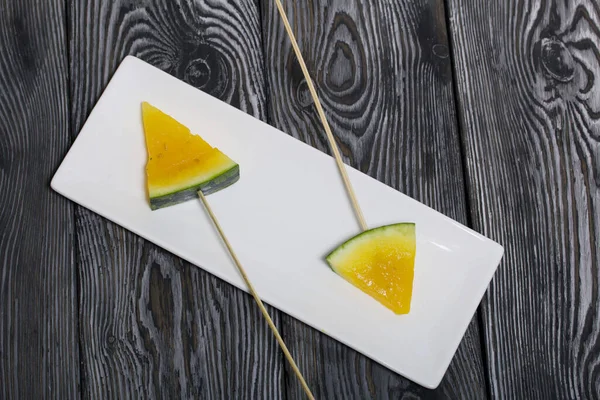 Şiş üzerinde sarı karpuz parçaları. Tabağa uzan. Tabak boyalı çam ağaçlarında.