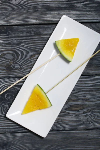 Şiş üzerinde sarı karpuz parçaları. Tabağa uzan. Tabak boyalı çam ağaçlarında.