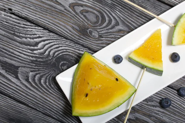 Çubuklardaki sarı karpuz parçaları. Tabağa uzan. Yakınlarda yabanmersini var. Tabak boyalı çam ağaçlarında.