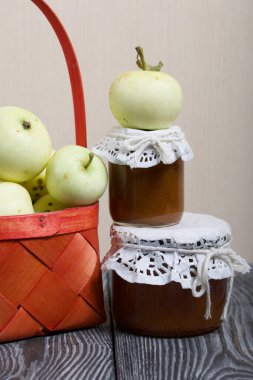 Kırmızı hasır sepetteki elmalar. Kavanozlarda reçel ve elmalar yakında. Meyve hasadı.