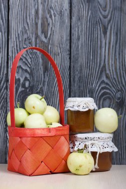 Kırmızı hasır sepetteki elmalar. Kavanozlarda reçel ve elmalar yakında. Meyve hasadı.