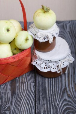 Kırmızı hasır sepetteki elmalar. Kavanozlarda reçel ve elmalar yakında. Meyve hasadı.