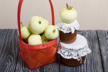 Kırmızı hasır sepetteki elmalar. Kavanozlarda reçel ve elmalar yakında. Meyve hasadı.