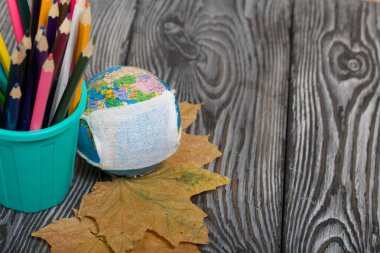 Kalem tutacağındaki renkli kalemler. Yakınlarda tıbbi maskeli ve kurumuş akçaağaç yapraklı bir küre var. Salgın sırasında akademik yıl.
