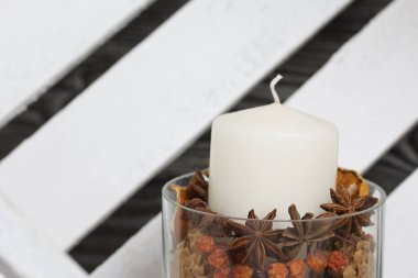 Cam şamdanda bir mum. Şamdan kurutulmuş koniler, baharatlar ve kurutulmuş meyvelerle dolu. Tahta bir kutunun içinde duruyor..