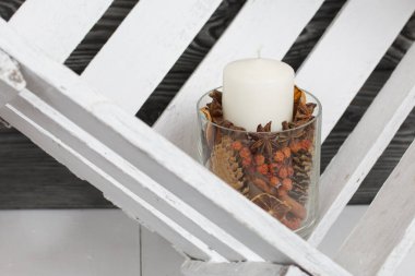 Cam şamdanda bir mum. Şamdan kurutulmuş koniler, baharatlar ve kurutulmuş meyvelerle dolu. Tahta bir kutunun içinde duruyor..