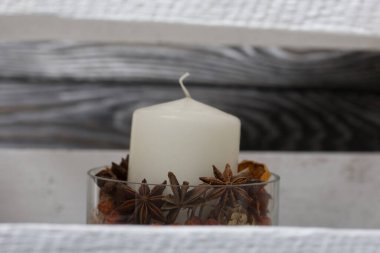 Cam şamdanda bir mum. Şamdan kurutulmuş koniler, baharatlar ve kurutulmuş meyvelerle dolu. Tahta bir kutunun içinde duruyor..